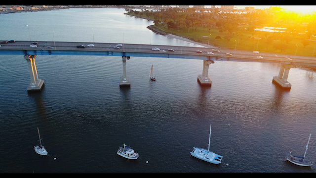 Golden Hour Sailboat crossing the Coronado Bridge with cars driving | Drone Video