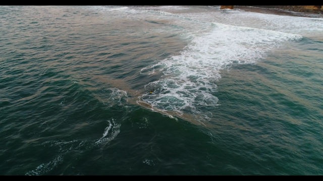 Aerial view of the cliffs, the surf and the ocean at Sunset Cliffs, with surfers out.