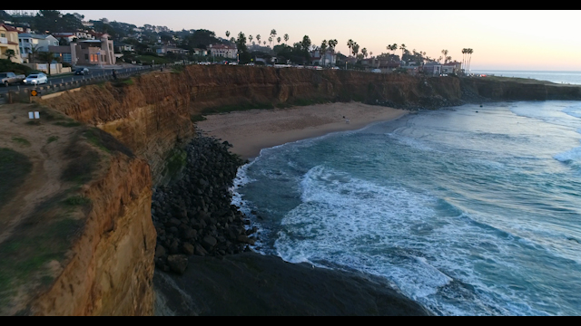 Low aerial view of the cliffs, the surf and palm trees at Sunset Cliffs.
