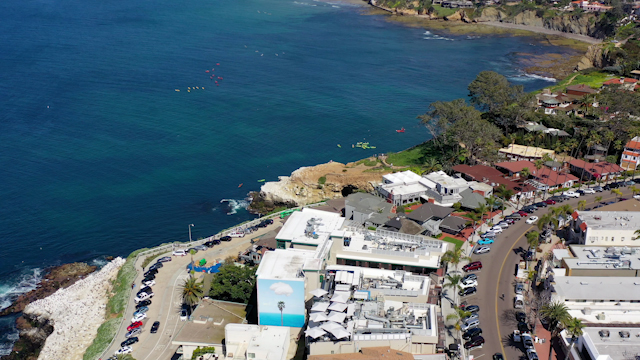 Aerial view of the cliffs, boats and the ocean at La Jolla Cove, with paddlers on the water.