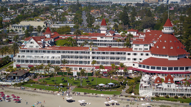 Aerial view of the beach, palm trees and the ocean at Hotel Del Coronado, with a crowd gathered.