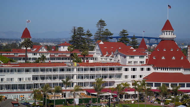 Low aerial view of the beach, the bridge and palm trees at Hotel Del Coronado, with people walking.