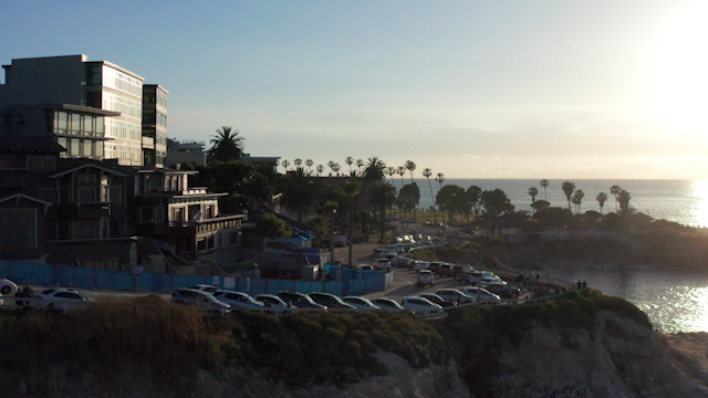 Low aerial view of the cliffs, palm trees and the ocean at La Jolla Cove, with people walking.