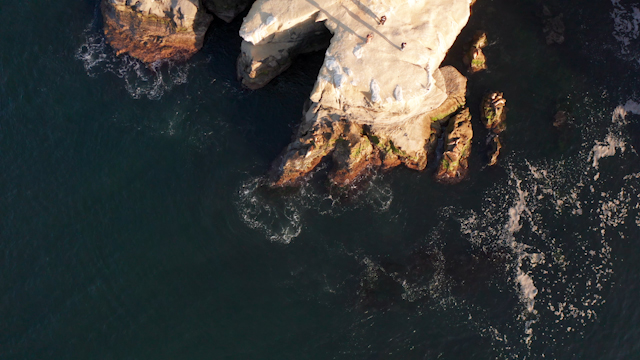 Aerial view of the cliffs, the surf and the ocean at La Jolla Cove, with people walking.
