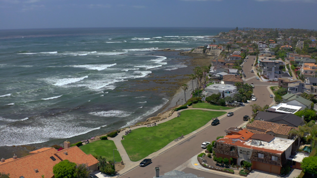 Aerial view of a residential street, the surf and palm trees at Bird Rock, with people walking.