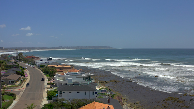 Low aerial view of a residential street, the surf and the pier at Bird Rock.