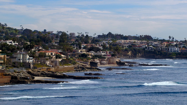 Low aerial view of a residential street, the surf and palm trees at Windansea.