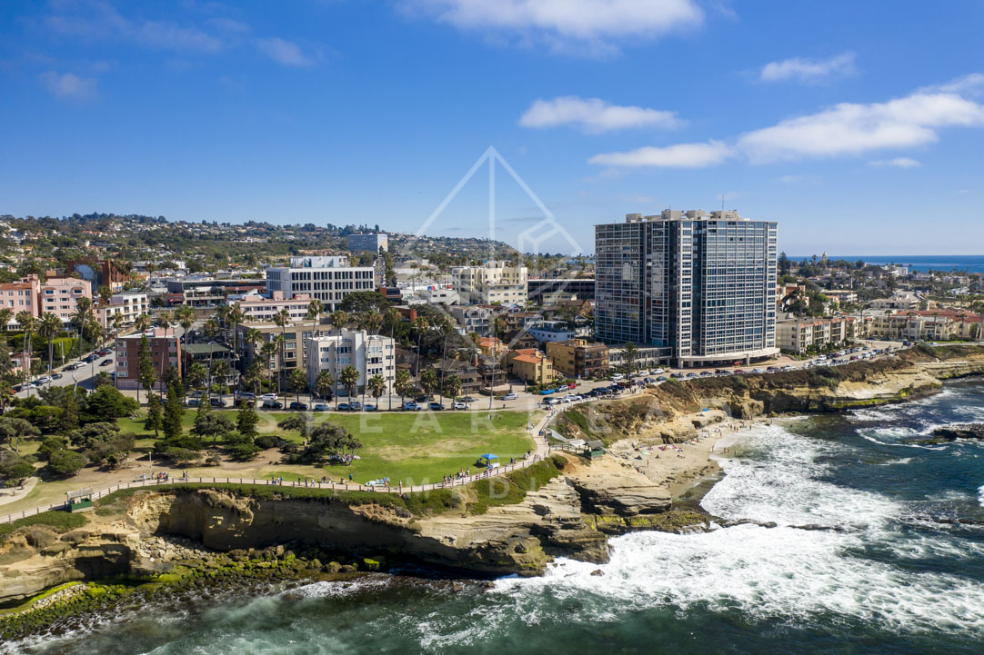 Aerial view of the cliffs, the surf and palm trees at La Jolla Cove, with people walking.