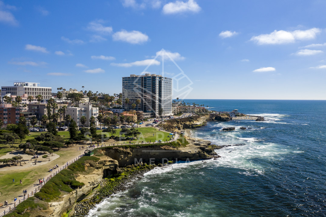 Aerial view of the cliffs, palm trees and the ocean at La Jolla Cove, with people walking.