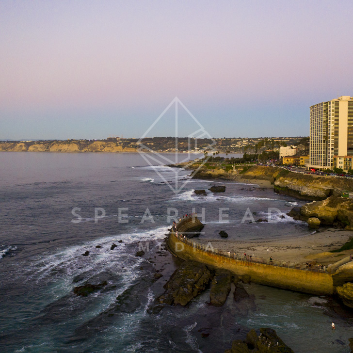 Aerial view of the cliffs, palm trees and the ocean at La Jolla Cove, with people walking.