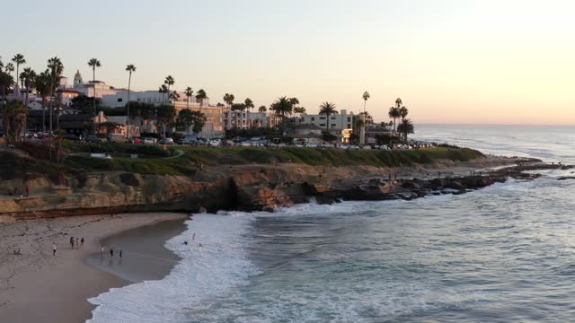 Aerial view of the cliffs, the surf and palm trees at La Jolla Cove, with people walking.