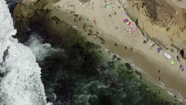 Aerial view of the beach, the surf and the ocean at La Jolla Cove, with a crowd gathered.