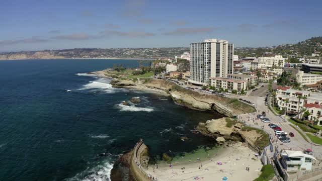 Aerial view of the cliffs, the ocean and homes at La Jolla Cove, with people walking.