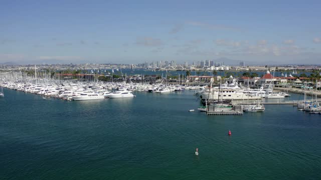 Low aerial view of the harbor, the skyline and boats in Point Loma, with paddlers on the water.