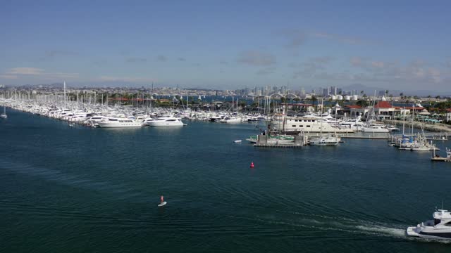 Low aerial view of the harbor, the skyline and boats in Point Loma, with paddlers on the water.