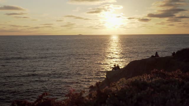 Elevated view of the cliffs, boats and the ocean at Sunset Cliffs, with a crowd gathered.