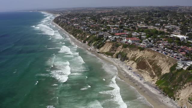 Aerial view of the cliffs, the surf and palm trees at Leucadia, with people walking.