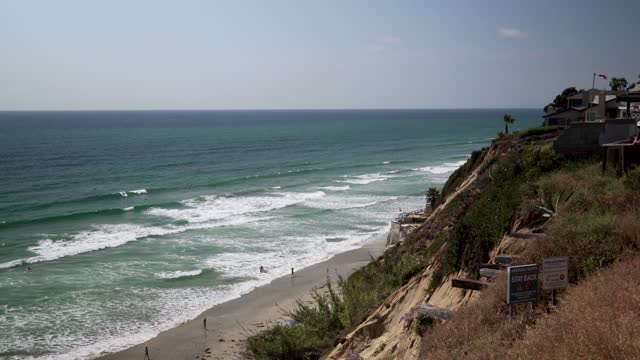 Elevated view of the cliffs, the surf and the ocean at Leucadia, with people walking.
