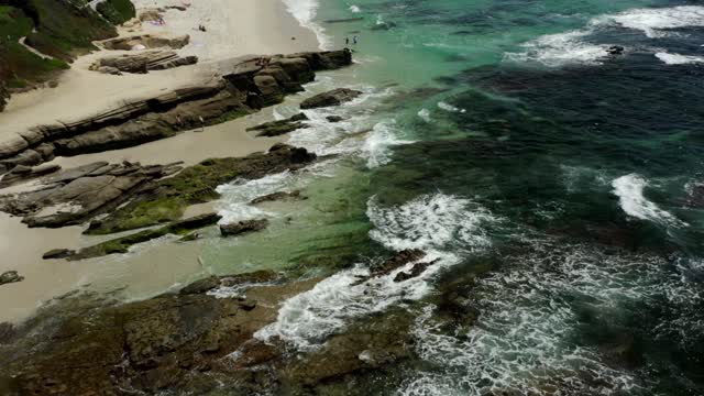 Aerial view of the beach, the surf and the ocean at Windansea, with people walking.