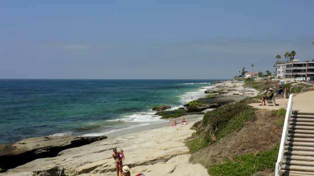 Elevated view of the beach, the surf and palm trees at Windansea, with people walking.