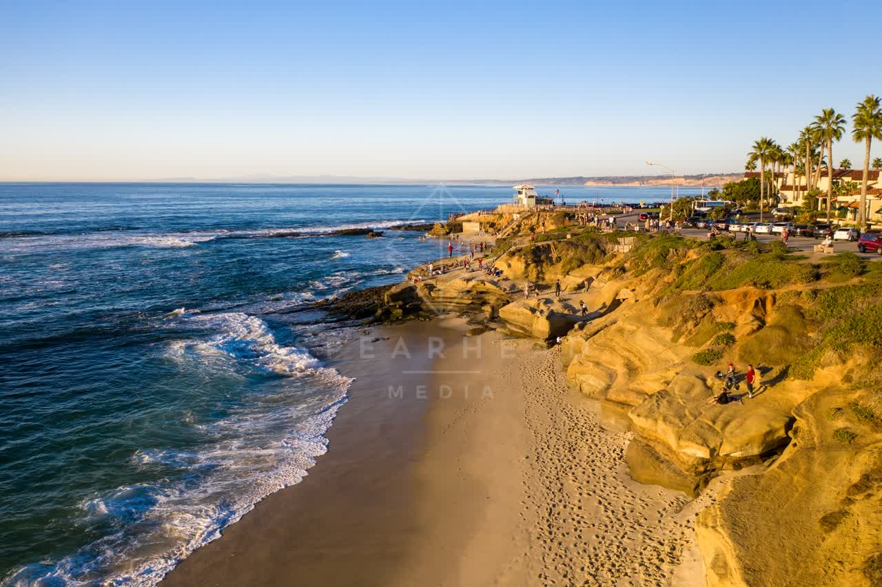 Low aerial view of the beach, the surf and palm trees at La Jolla Cove, with people walking.