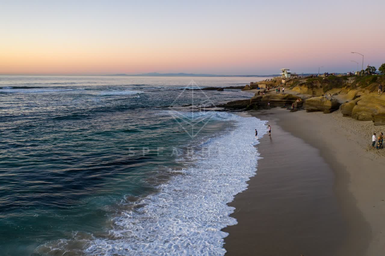 Low aerial view of the beach, the surf and the ocean at La Jolla Cove, with people walking.