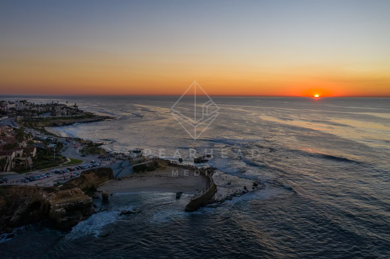 Aerial view of the cliffs, the ocean and homes at La Jolla Cove, with a crowd gathered.