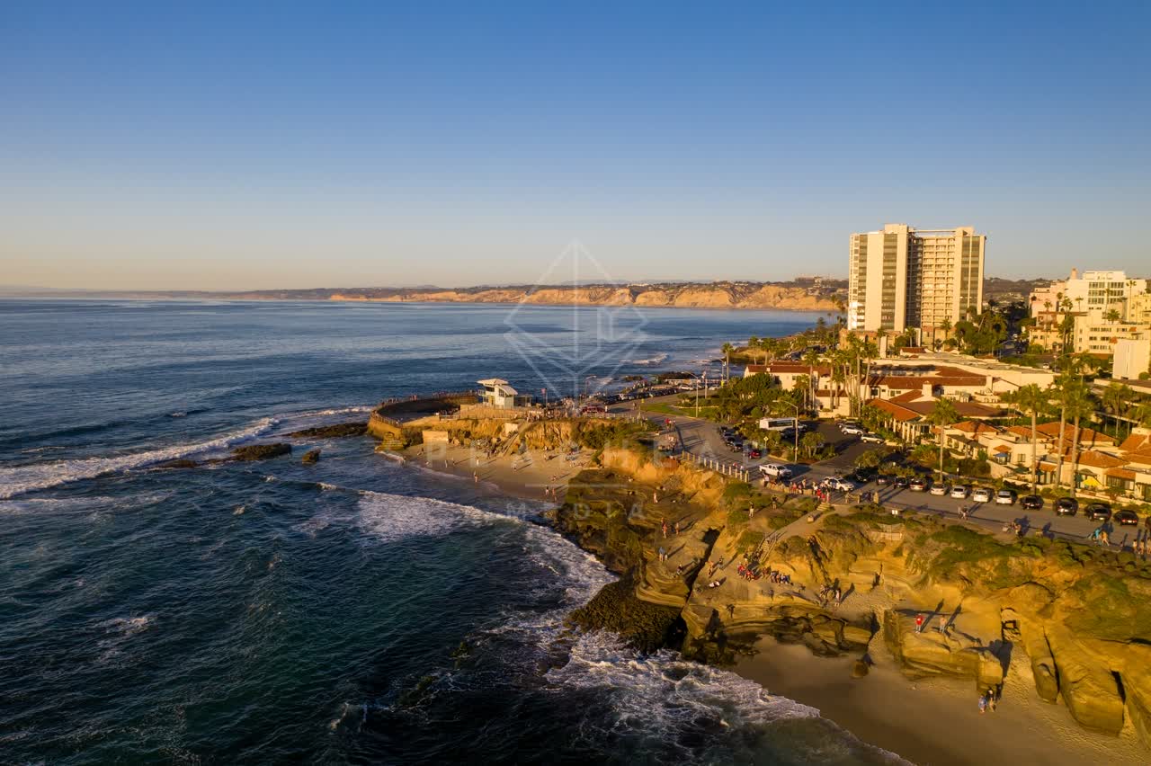 Aerial view of the cliffs, the surf and palm trees at La Jolla Cove, with people walking.