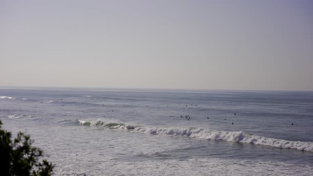 Elevated view of the cliffs, the surf and the ocean at Bird Rock, with surfers out.