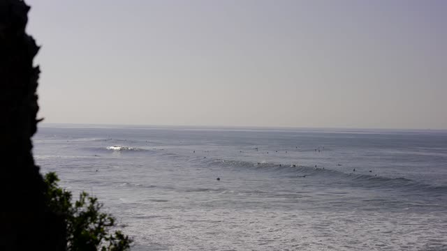 Elevated view of the cliffs, the surf and the ocean at Bird Rock, with surfers out.