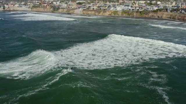 Aerial view of the cliffs, the surf and the ocean at Bird Rock, with surfers out.