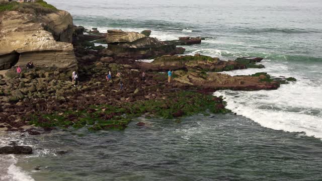 Elevated view of the cliffs, the surf and the ocean at La Jolla Cove, with people walking.