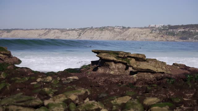 The cliffs, the surf and boats at La Jolla Cove, with surfers out.