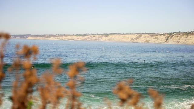 Elevated view of the cliffs, the surf and the ocean at La Jolla Cove, with swimmers in the water.