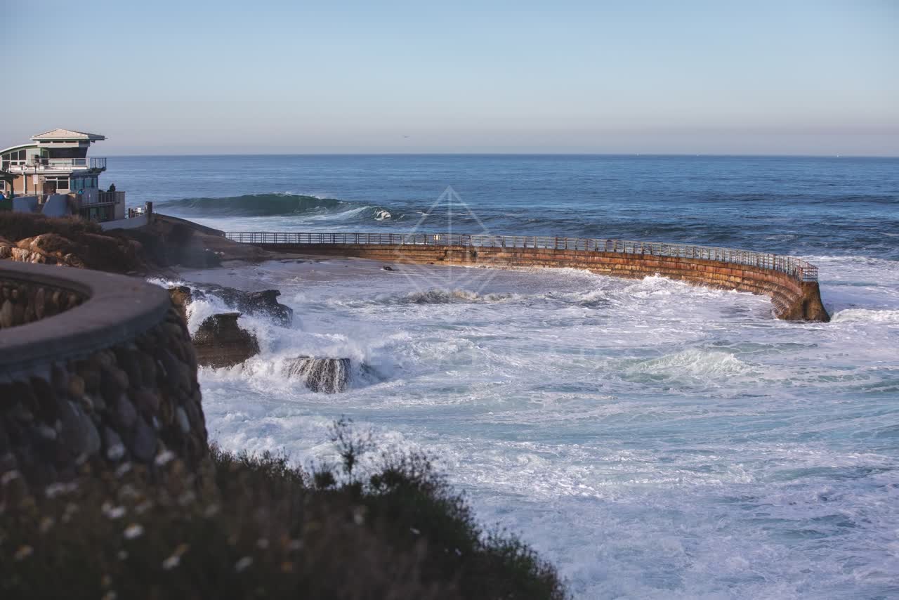 Elevated view of the cliffs, the surf and the ocean at La Jolla Cove, with people walking.
