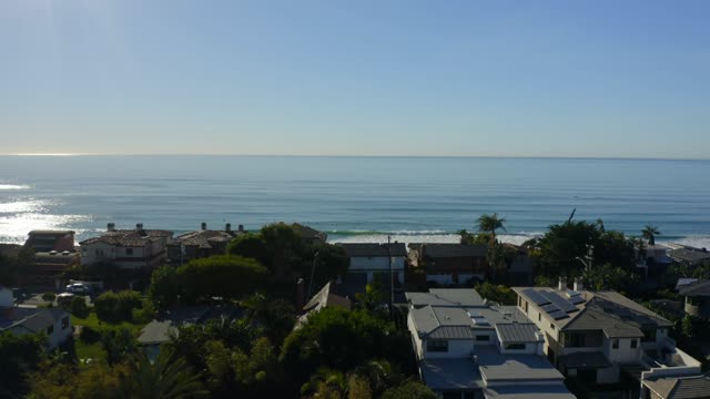 Low aerial view of a residential street, the surf and palm trees at Leucadia.