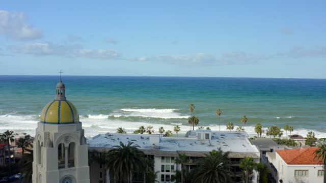 Low aerial view of a residential street, the surf and palm trees at La Jolla Cove.