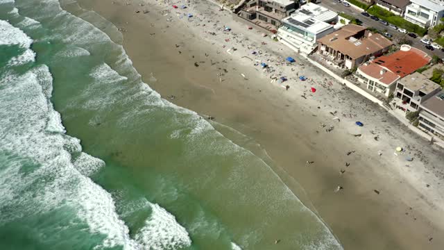 Aerial view of the beach, the surf and the ocean at La Jolla Cove, with a crowd gathered.
