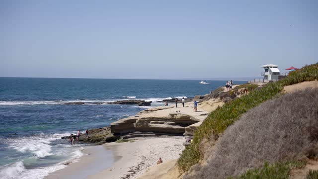 Elevated view of the cliffs, boats and the ocean at La Jolla Cove, with people walking.