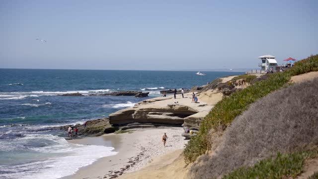 Elevated view of the beach, the surf and the ocean at La Jolla Cove, with people walking.
