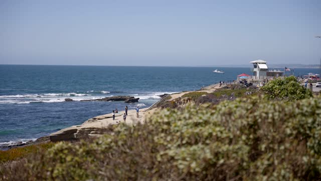 Elevated view of the cliffs, boats and the ocean at La Jolla Cove, with people walking.