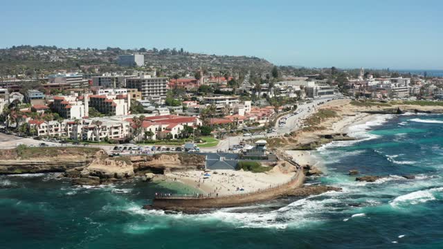 Aerial view of the cliffs, palm trees and the ocean at La Jolla Cove, with people walking.