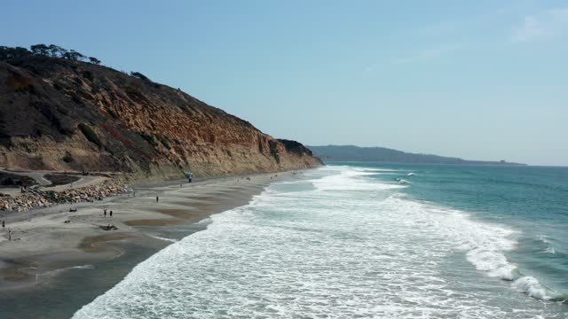 Low aerial view of the cliffs, the surf and the ocean at Torrey Pines, with people walking.