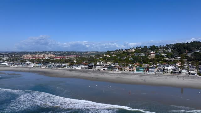 Low aerial view of the beach, the surf and palm trees at Powerhouse Park, with people walking.
