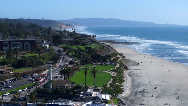 Aerial view of the beach, the surf and palm trees at Powerhouse Park, with people walking.