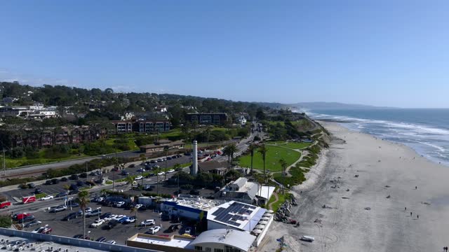 Aerial view of the beach, the surf and palm trees at Powerhouse Park, with people walking.