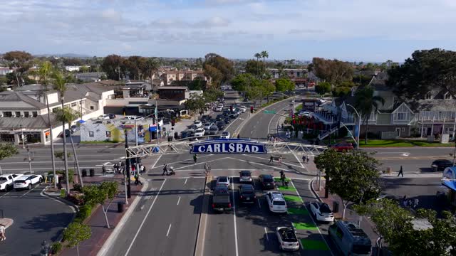 Low aerial view of the downtown streets, palm trees and the buildings in Carlsbad, with people walking.
