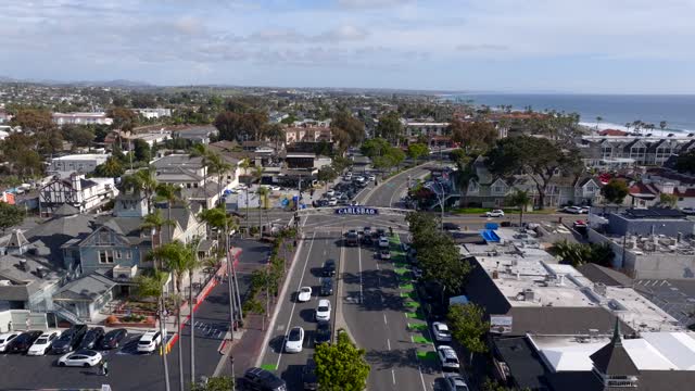 Low aerial view of the downtown streets, palm trees and the ocean in Carlsbad, with people walking.