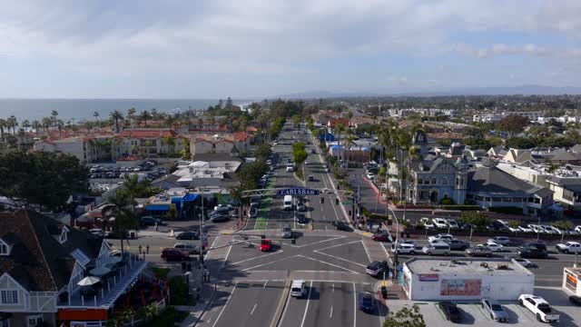 Low aerial view of the downtown streets, palm trees and the ocean in Carlsbad, with people walking.