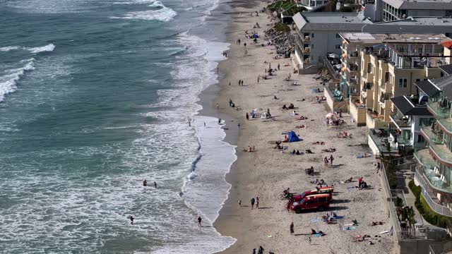 Aerial view of the beach, the surf and the ocean in Carlsbad, with a crowd gathered.